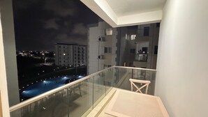 A balcony with a glass railing, a table, and a chair, overlooking a cityscape at night. - The 401 Apartment (Tema)