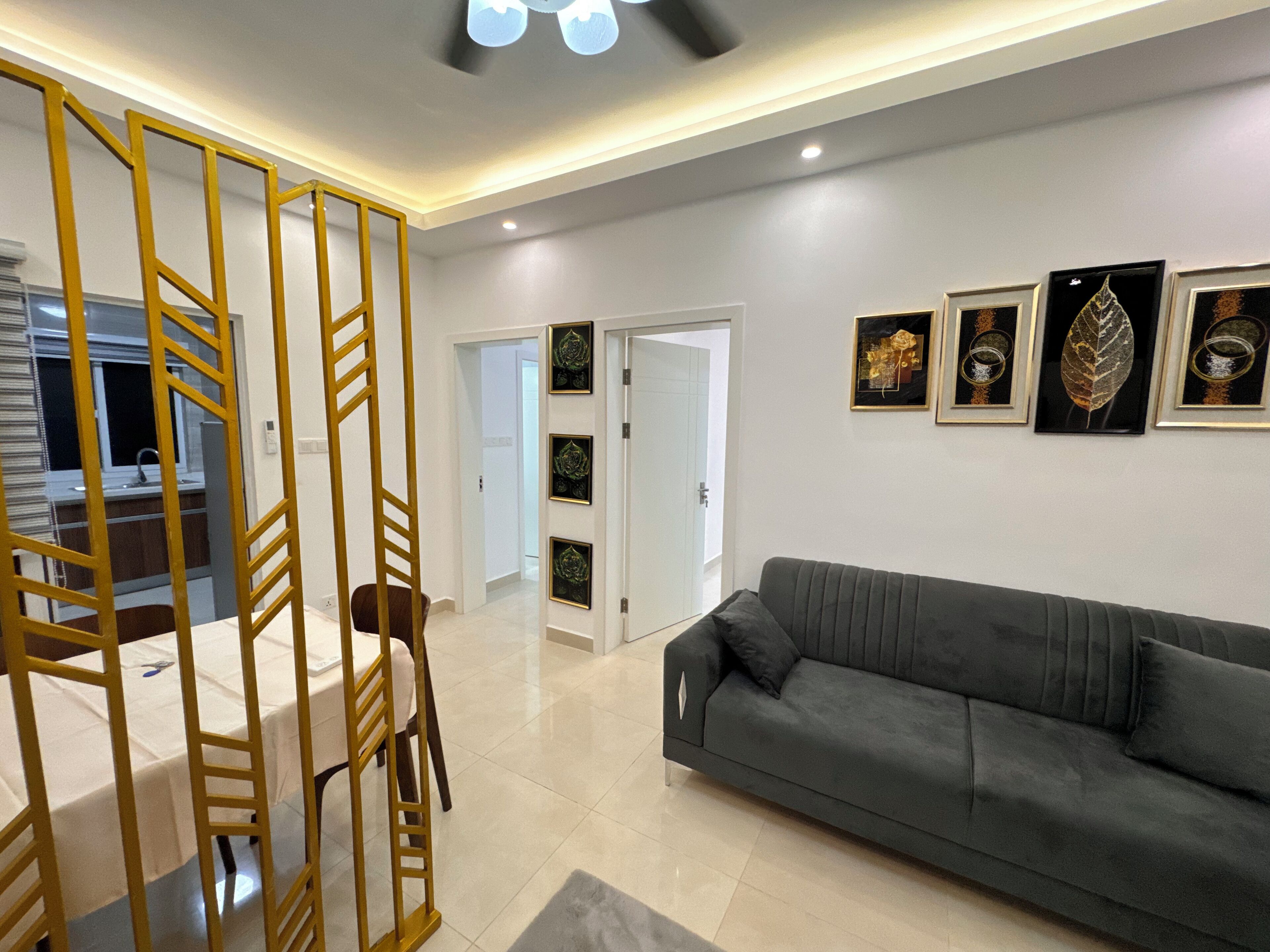 A modern living room with a grey sofa, a wooden partition, and framed botanical prints on the wall.