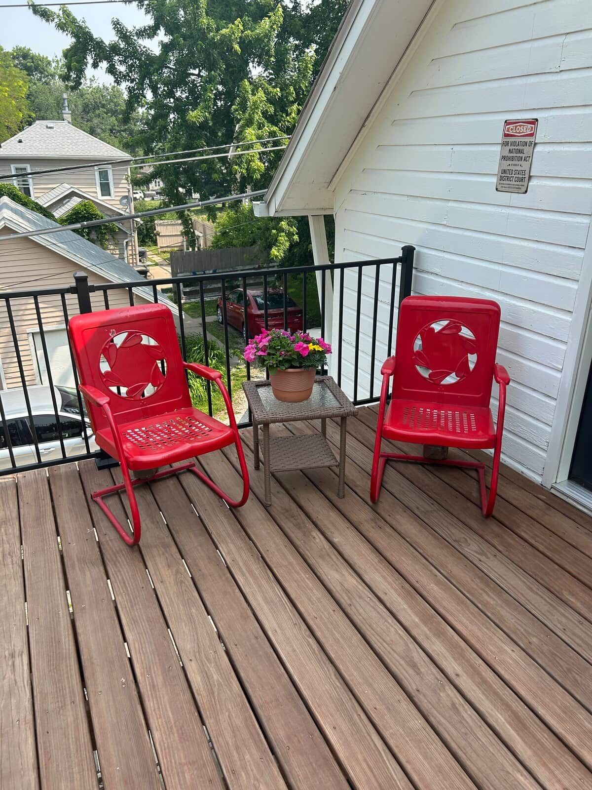 A wooden deck with two red chairs and a potted plant.