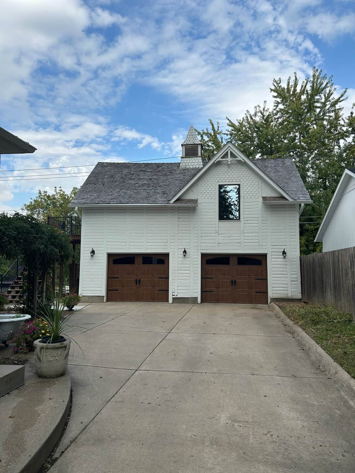 A two-story white building with a gabled roof and a central chimney. There are two garage doors and a small window on the second floor.