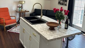 A modern kitchen with a central island, a black sofa, and a dining area with a black chair.