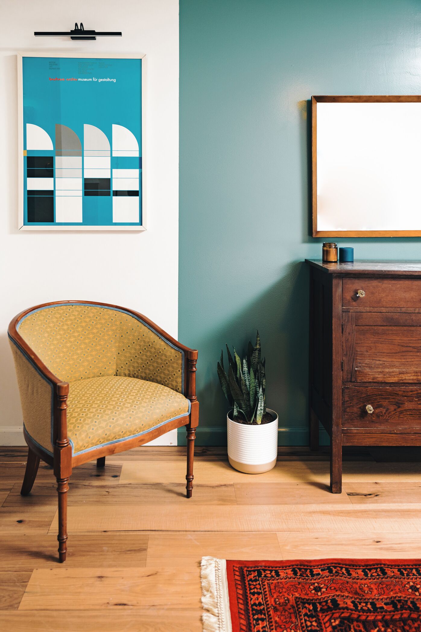 Una habitación con una silla de madera, un armario blanco, una planta en maceta y un cuadro en la pared.