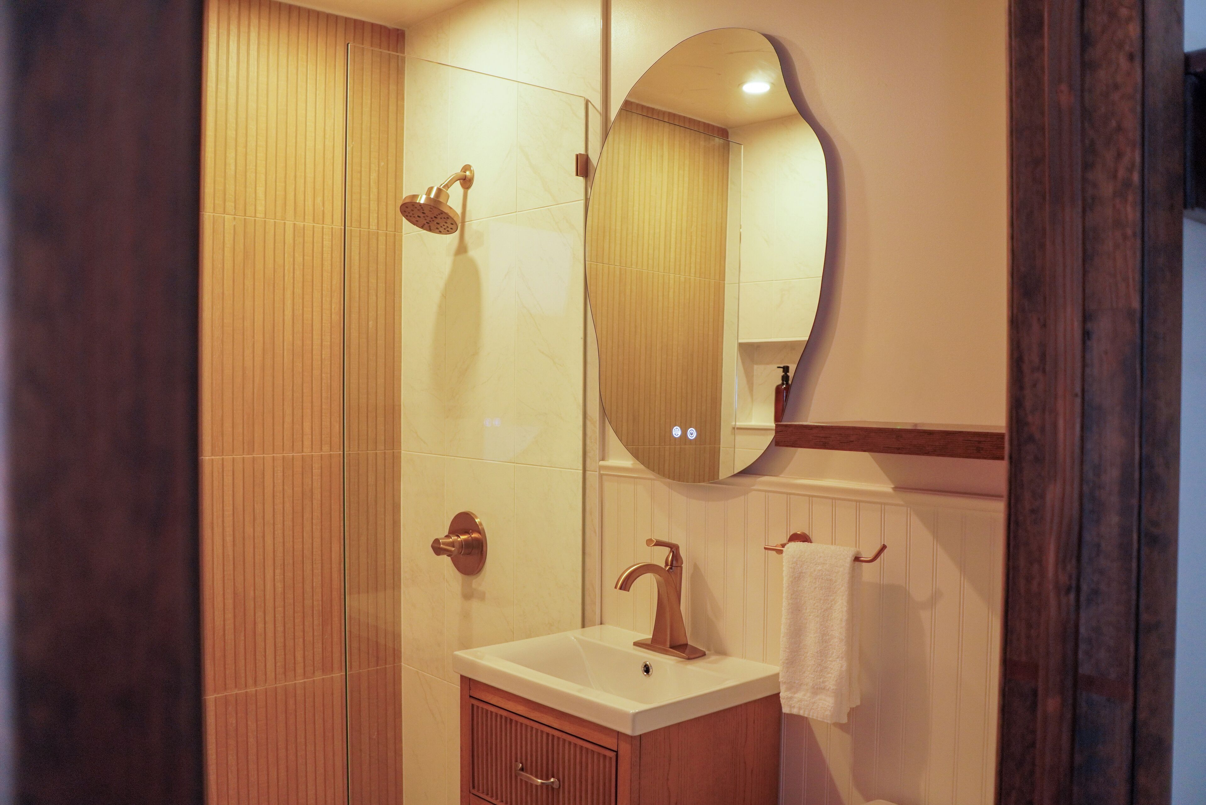 A bathroom with a wooden vanity, a sink, a mirror, and a shower.