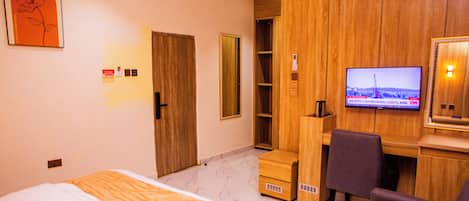 A hotel room with a bed, a desk with a chair, a television, and a wardrobe.