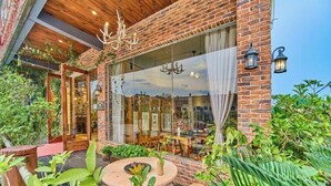 A brick building with a glass door entrance, outdoor seating area, and potted plants. - Danxia Mountain Fengqing Hostel (Renhua)