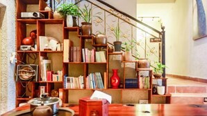A cozy reading nook with a wooden bookshelf filled with books and decorative items, a small table with a teapot, and a staircase with a metal railing. - Danxia Mountain Fengqing Hostel (Renhua)