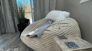 A modern bedroom with a large, curved bed, a small side table, and a potted plant. - Treehouse Farm Stay on the Maine Coast (Harpswell)
