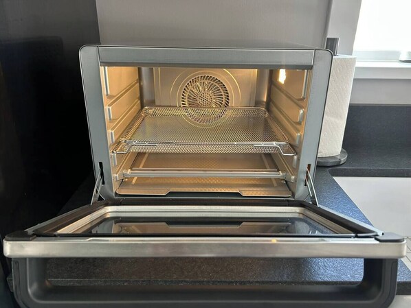 Forno aberto com uma grade metálica interna, um ventilador na parte de trás e uma bancada preta abaixo.