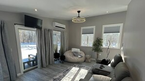 A modern living room with a sofa, bean bag, and a large window. - Treehouse Farm Stay on the Maine Coast (Harpswell)
