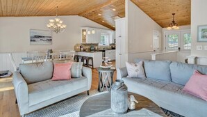 A spacious living area with a wooden ceiling, two grey sofas with pink cushions, a round coffee table, and a kitchen in the background. - Welcome to Playcation - fun for all ages! (Moneta)