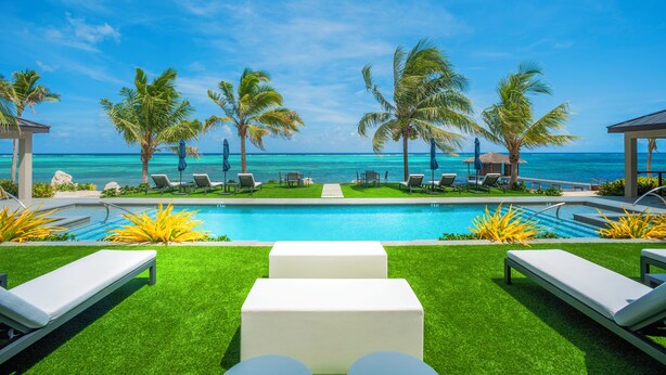 Un espace aménagé au bord de la piscine, avec des chaises longues, des palmiers et une vue sur l’océan.