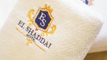 A white towel with embroidered text and a logo, indicating it is from El Shaddai Hotel.
