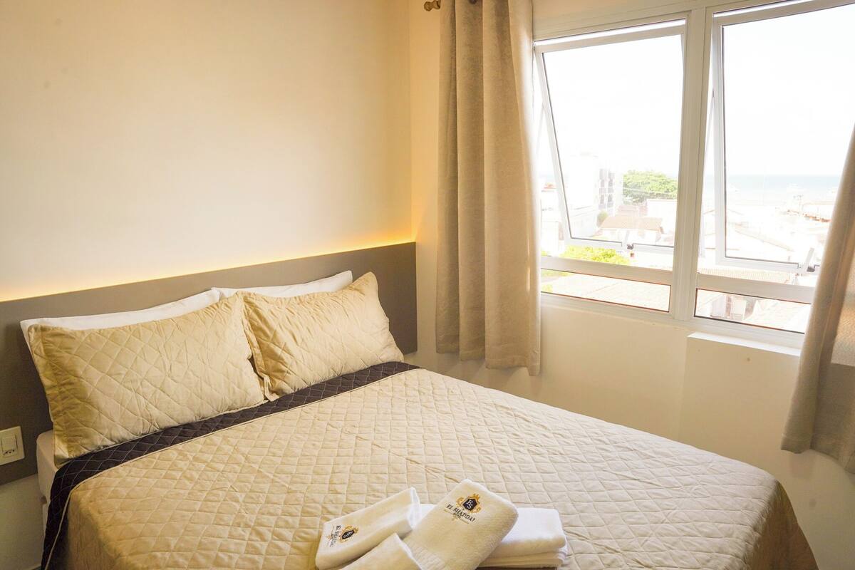 A neatly made bed with a quilted cover, two pillows, and a set of towels on the side.