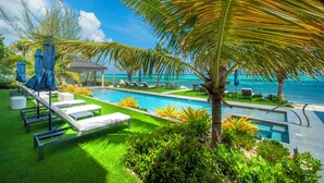 A pool area with lounge chairs, a small gazebo, and a palm tree. - 3 Bedroom Luxury Oceanfront Condo (Bodden Town)