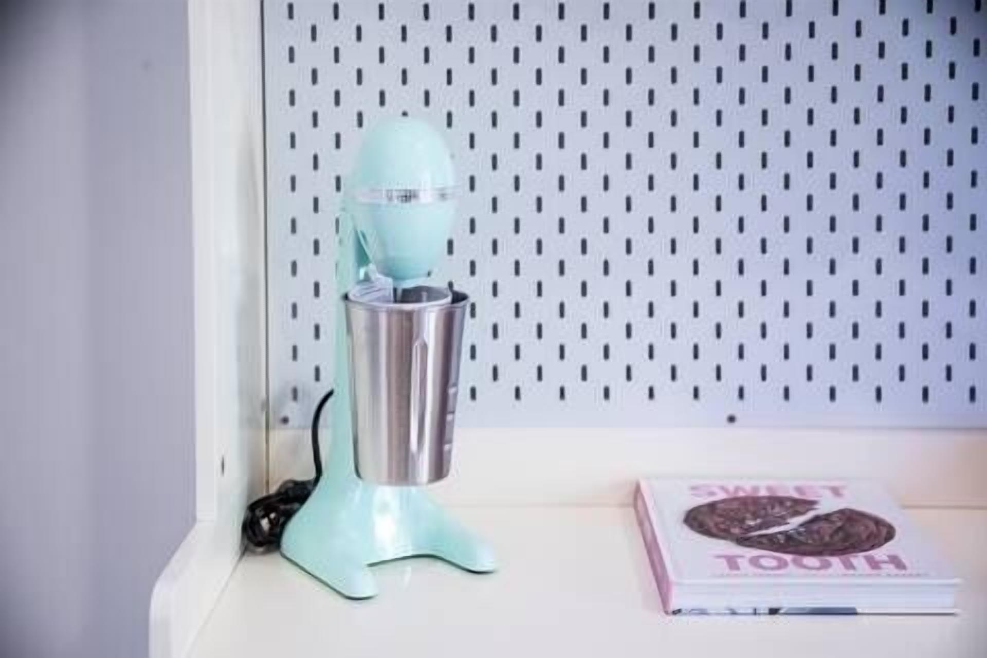 A kitchen area with a teal-colored appliance, a white wall with a dotted pattern, and a book titled "SWEET TOOTH" on a surface.