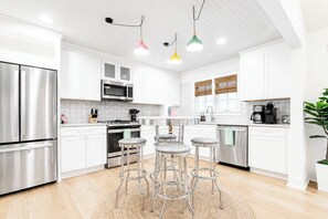 Une cuisine moderne dotée d’appareils électroménagers en acier inoxydable, de meubles blancs et d’un îlot central avec des tabourets de bar.
