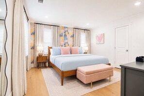 A bedroom with a bed, bedside tables, a bench, a door, and a wall with a heart-shaped decoration.