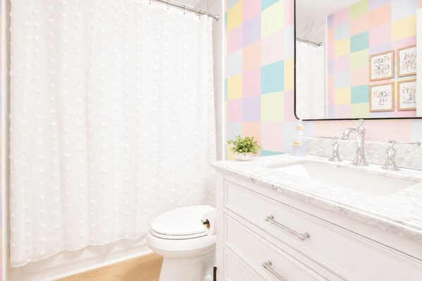 A bathroom with a toilet, a shower curtain, a sink with a mirror, and a wall with colorful square tiles.