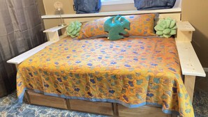 Una cama con colcha estampada de flores, dos almohadas verdes y una mesita de noche con lámpara.