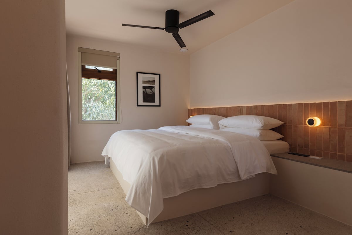 A bedroom with a bed, a ceiling fan, a window, and a wall-mounted light fixture.