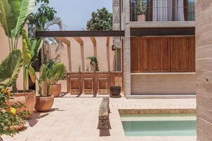 Un área de piscina con piso de baldosas, bancos de madera y plantas en macetas.