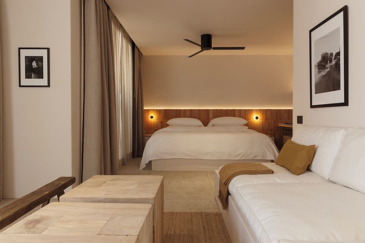 A hotel room with two beds, a ceiling fan, a wooden headboard, and a framed picture on the wall.