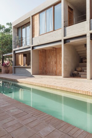 Una casa moderna de dos pisos con piscina, ventanas amplias y un balcón.
