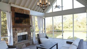 Una sala de estar con ventanales, chimenea de piedra y ventilador de techo.