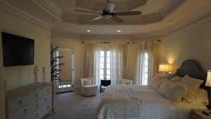 Un dormitorio con una cama grande, un ventilador de techo, un televisor montado en la pared y un aparador.
