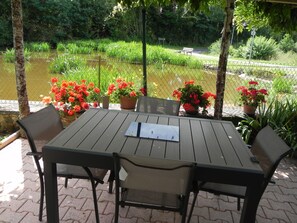 An outdoor patio with a table and chairs, surrounded by potted plants and a pond.