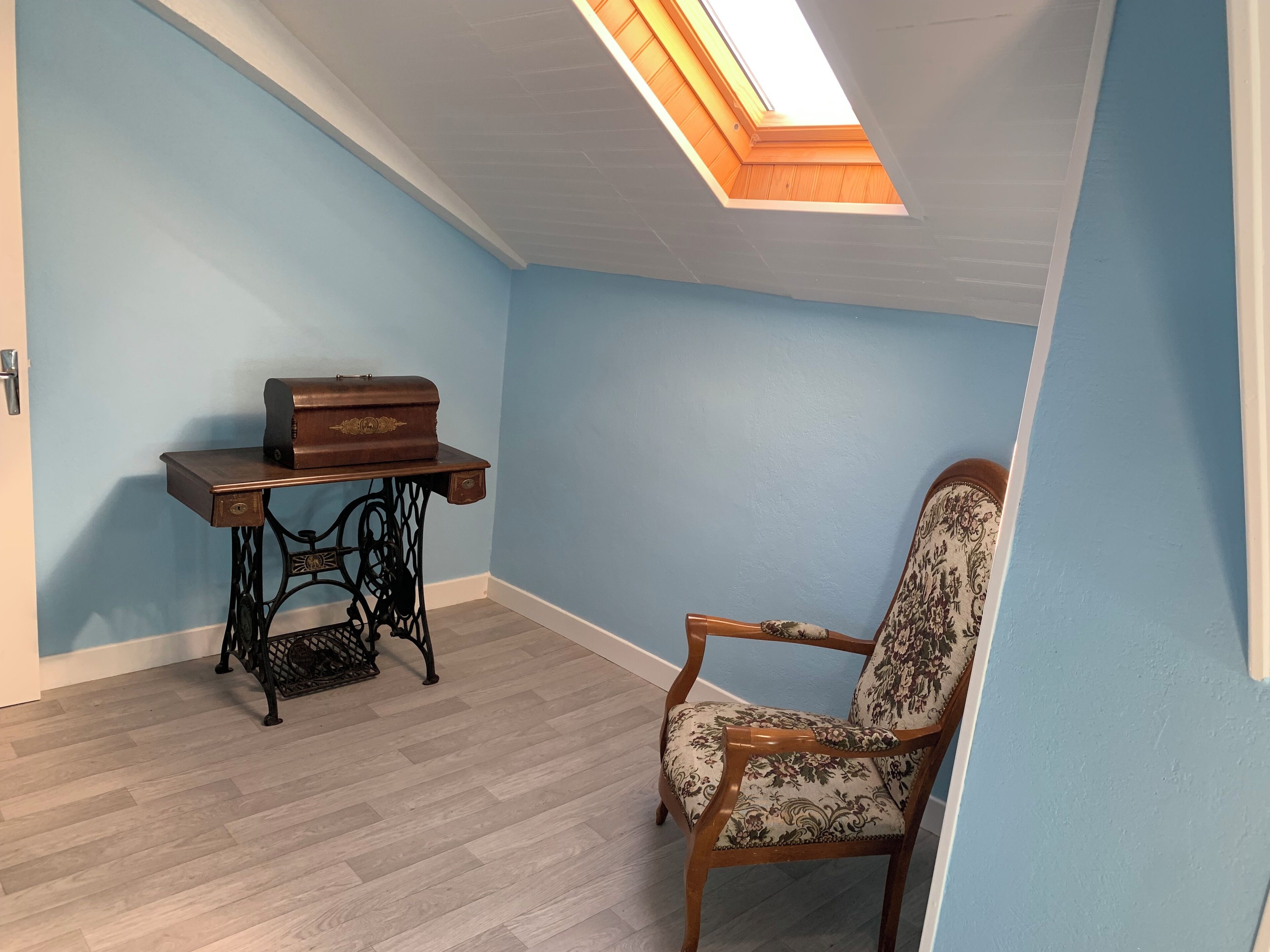 A room with a skylight, a sewing machine on a table, and a patterned chair.