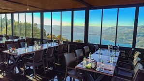 Een restaurant met grote ramen en een prachtig uitzicht op bergen en een meer. Tafels zijn gedekt met waterflesjes en toevoegingen.
