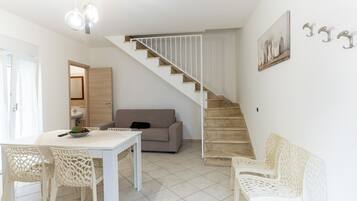 Un intérieur moderne comprenant un escalier, un coin repas avec une table et des chaises, un canapé et une œuvre d’art accrochée au mur.