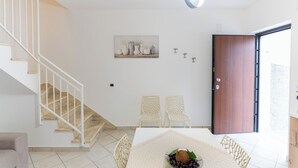 Un intérieur moderne avec un escalier, deux fauteuils en osier, une porte en bois et une table à manger agrémentée d’un panier de fruits.