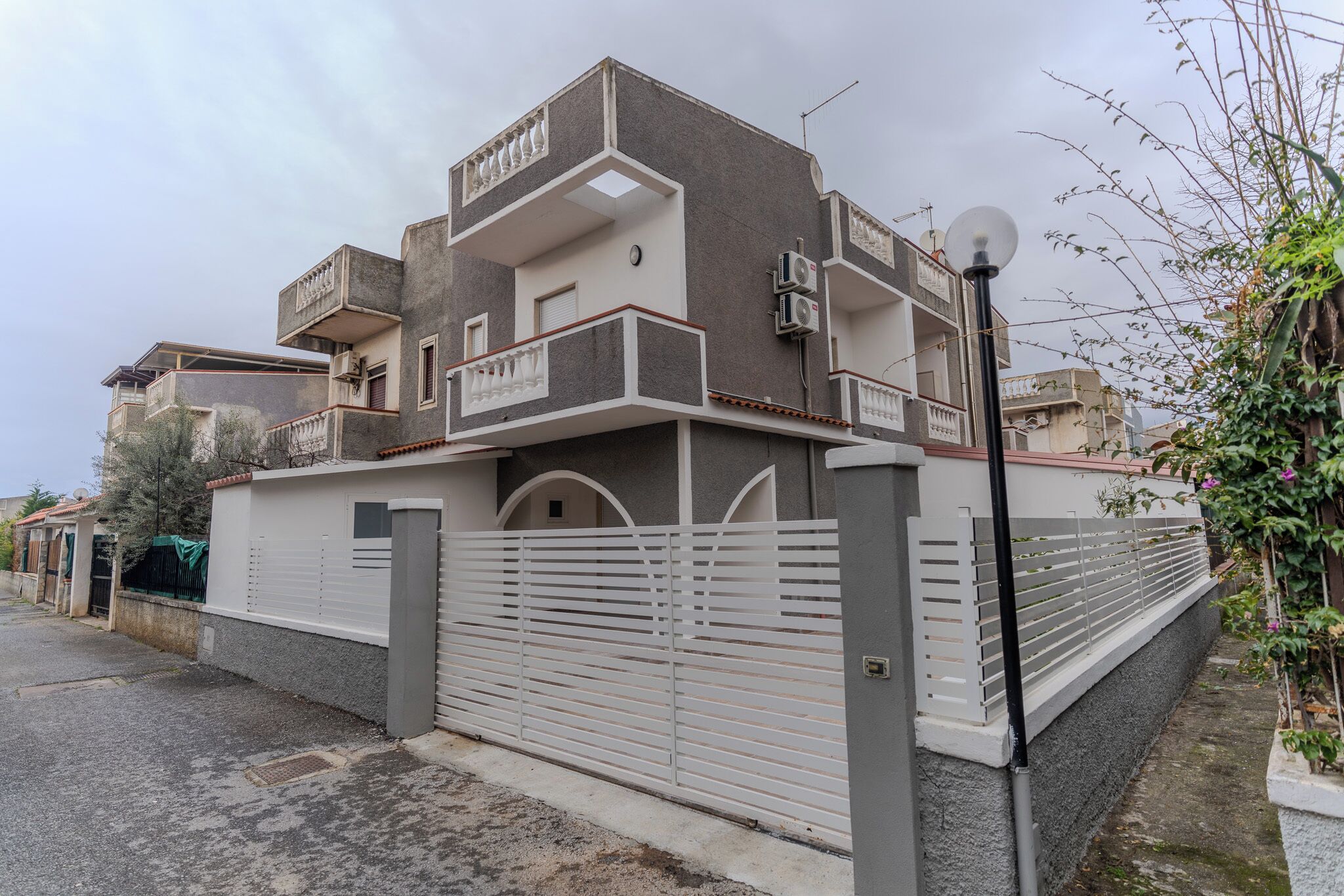 Een modern huis met twee verdiepingen, een balkon, een hek en uitzicht op de straat.