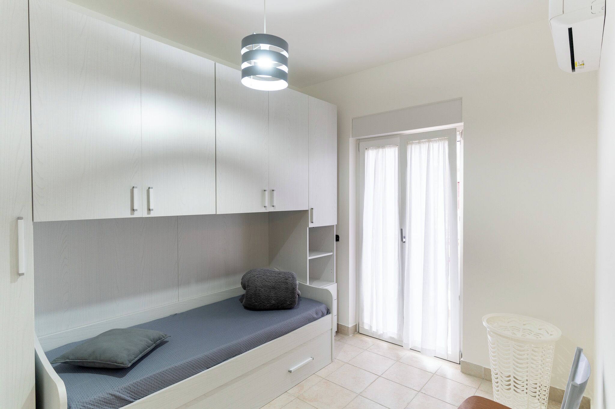 Ein Schlafzimmer mit Bett, Kleiderschrank, Pendelleuchte und einem fenster mit Vorhängen.