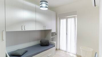Ein Schlafzimmer mit Bett, Kleiderschrank, Pendelleuchte und einem fenster mit Vorhängen.