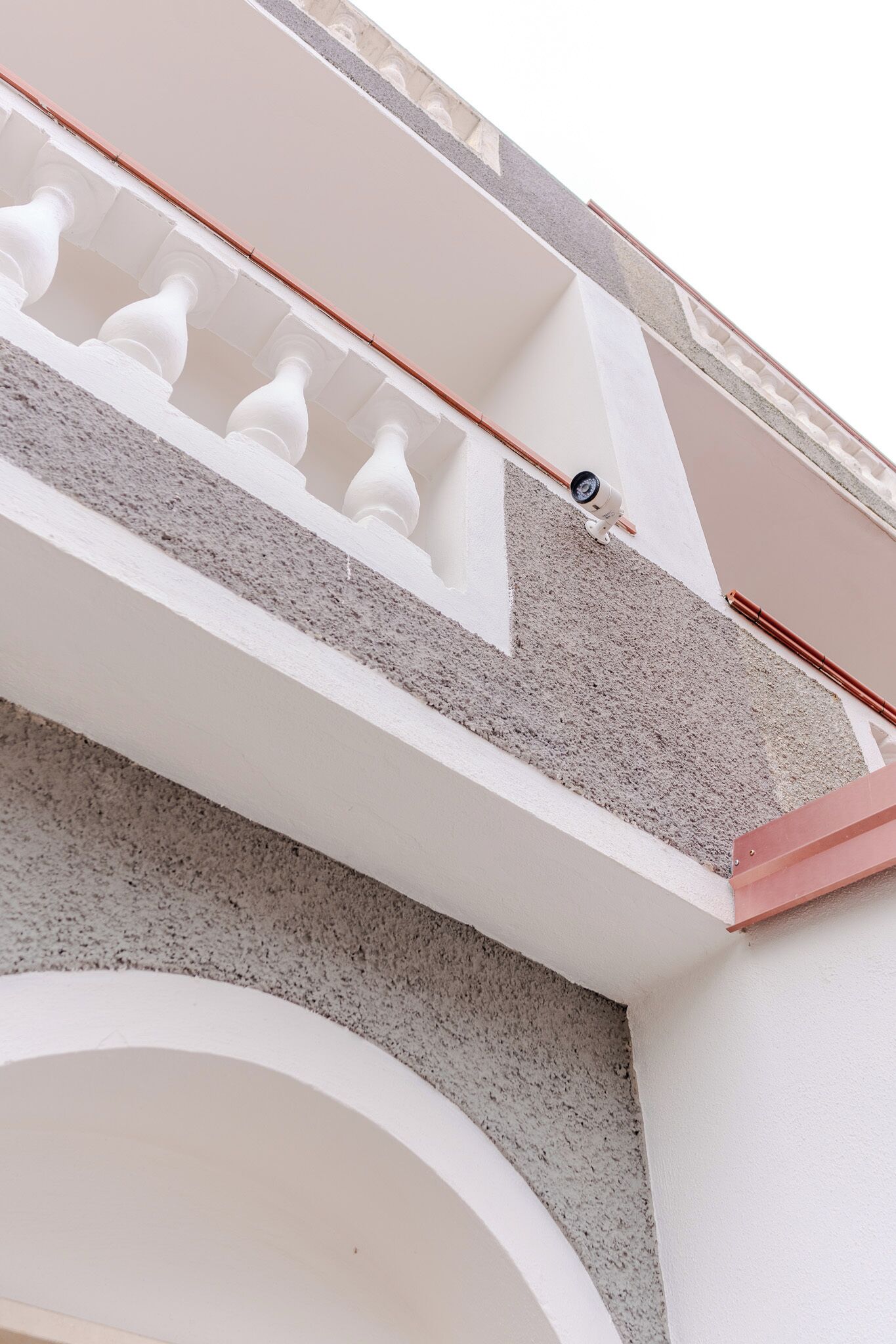 A modern architectural design with a white and grey color scheme, featuring a balcony with white balustrades and a grey textured wall.
