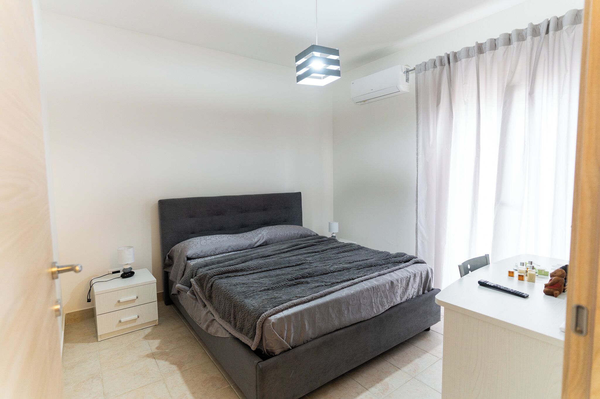 Een slaapkamer met een bed, nachtkastje, lamp en een bureau met stoel.