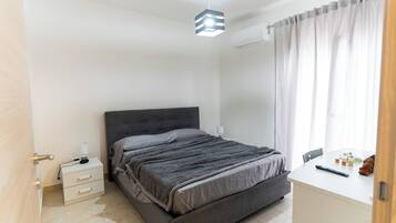 Een slaapkamer met een bed, nachtkastje, lamp en een bureau met stoel.