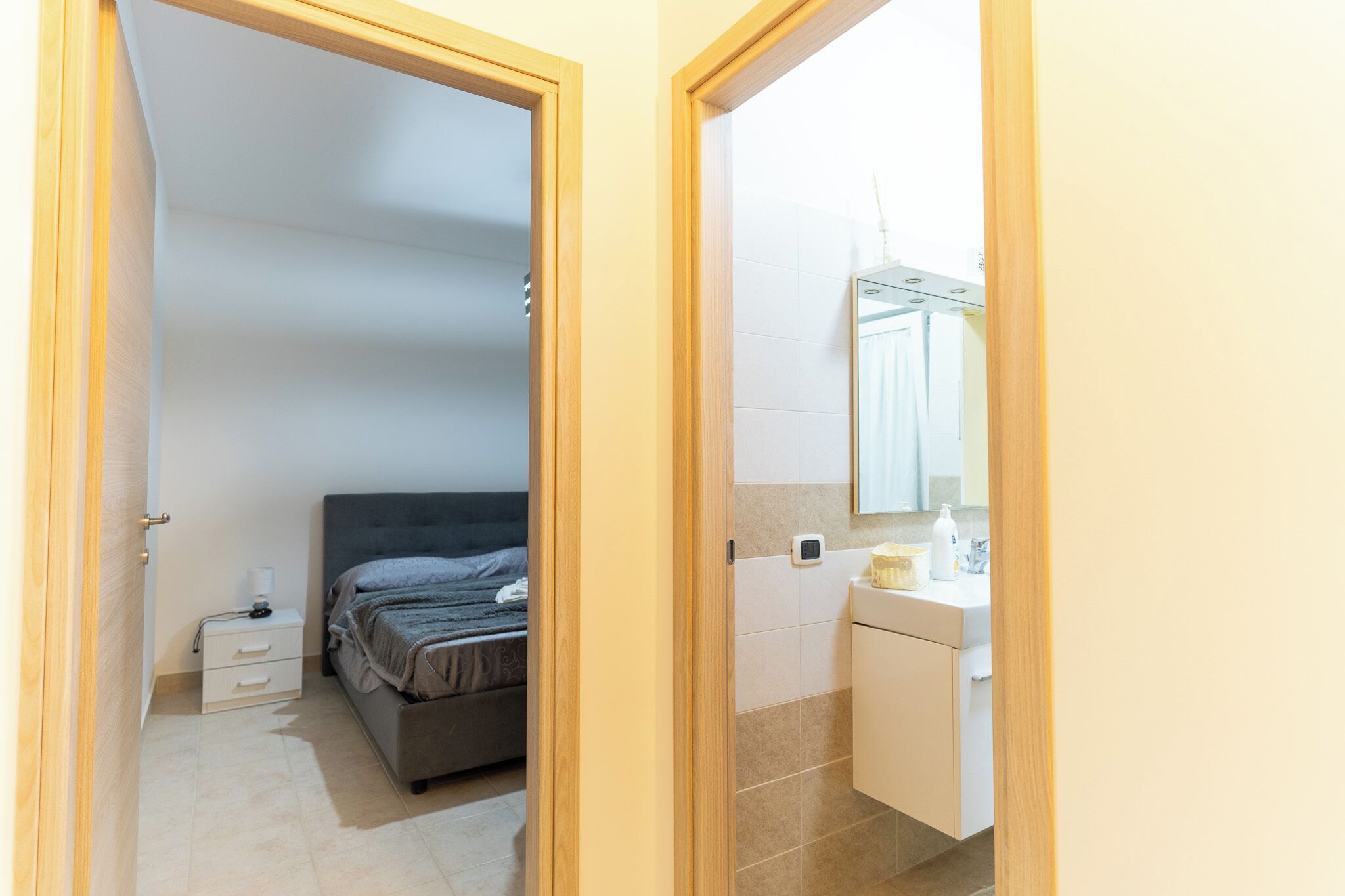 Une chambre à coucher avec un lit, une table de chevet et une commode. Il y a une salle de bain avec un lavabo, un miroir et des articles de toilette.