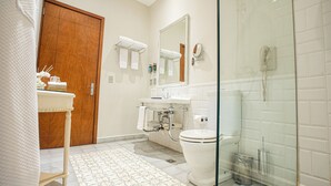 Un bany amb porta de fusta, plat de dutxa de vidre, un lavabo blanc amb mirall i un paviment amb dibuixos.
