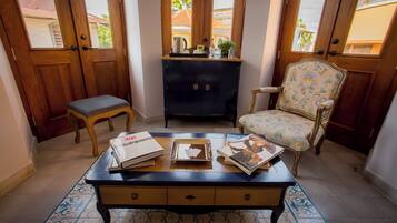 A room with a wooden bench, a desk with books and a tray, a decorative chair, and a cabinet with items on top.