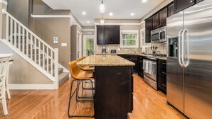 A modern kitchen with a central island, stainless steel appliances, and a staircase leading to another level.
