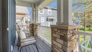 A covered porch with wicker chairs, a stone fireplace, and a view of neighboring houses.