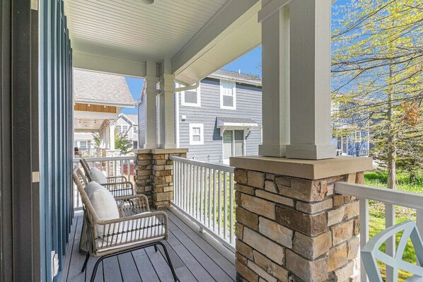 A covered porch with wicker chairs, a stone fireplace, and a view of neighboring houses.