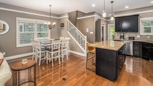 A modern kitchen with a central island, white dining set, and a staircase leading to another level.