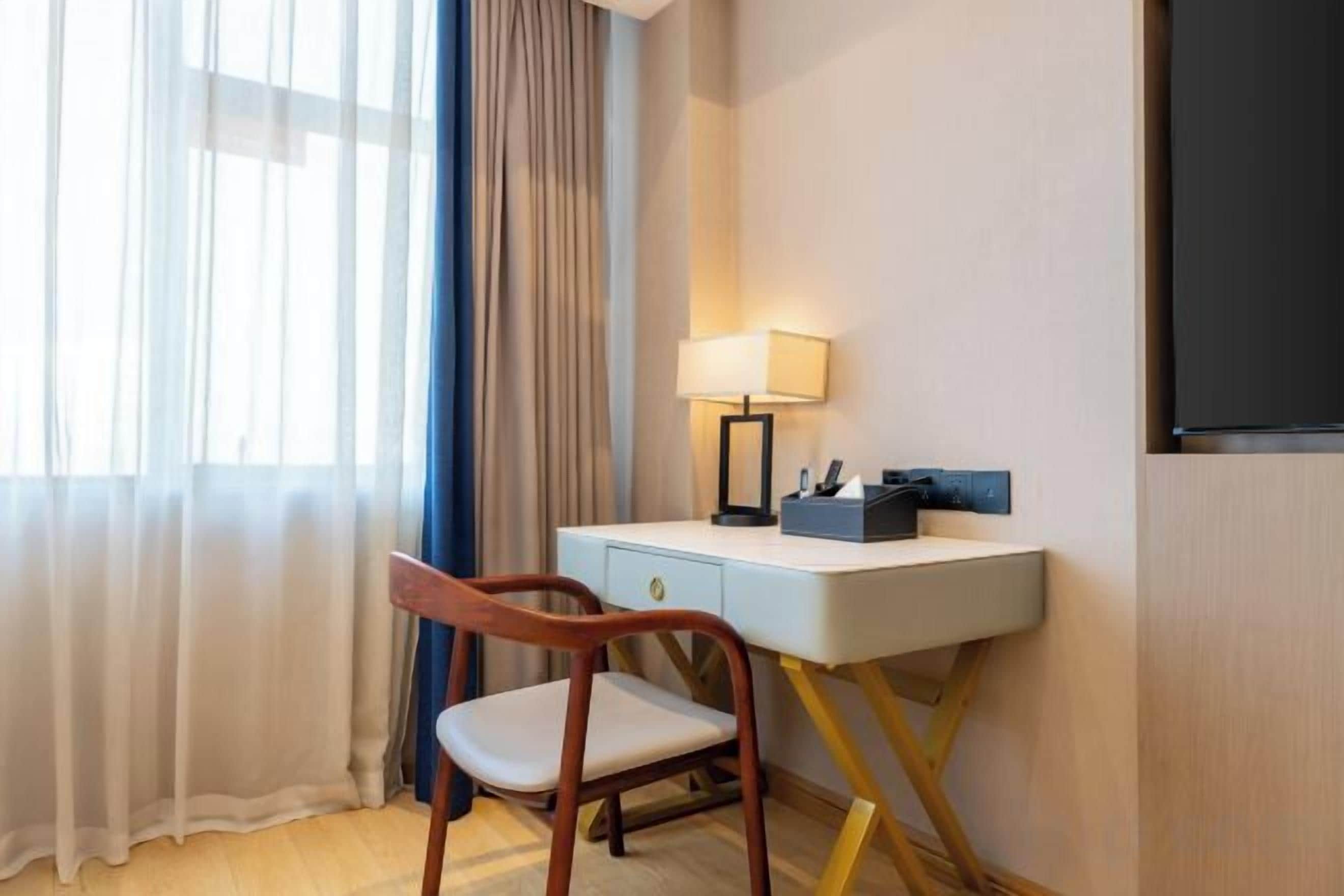 A hotel room with a desk, chair, lamp, and a television.
