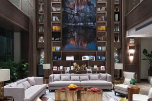 A spacious living area with a large sofa, a coffee table, and a bookshelf filled with books and decorative items. - Huace American Hotel (Shenzhen Longgang Shuanglong Subway Station) (Shenzhen)