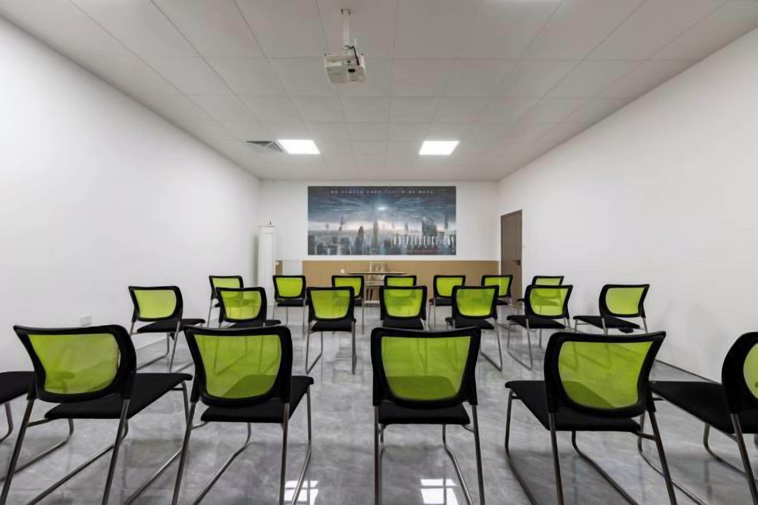 A conference room with rows of chairs, a projector, and a cityscape poster on the wall.